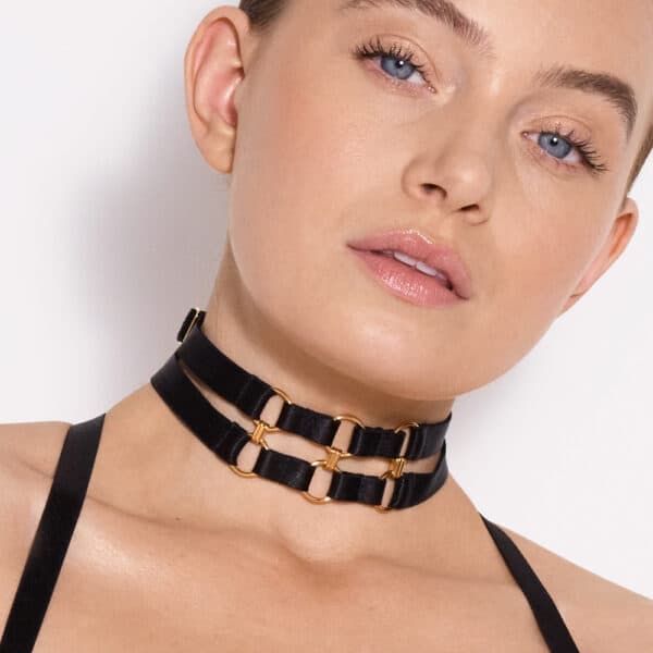 a blue-eyed woman wears a black two-strap necklace that connects to a gold circle