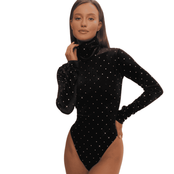 A woman stands elegantly in front of a white wall, wearing a black velvet turtleneck bodysuit. This refined garment is enhanced by the meticulous inlaying of Swarovski crystals, adding a touch of brilliance and sparkle to her outfit. The combination of dark velvet and sparkling crystals creates a captivating visual contrast, highlighting sophistication and attention to detail in her wardrobe choices. This unique combination of textures and decorative elements lends the ensemble a chic, modern allure, capturing attention and reflecting the woman's refined taste in fashion.