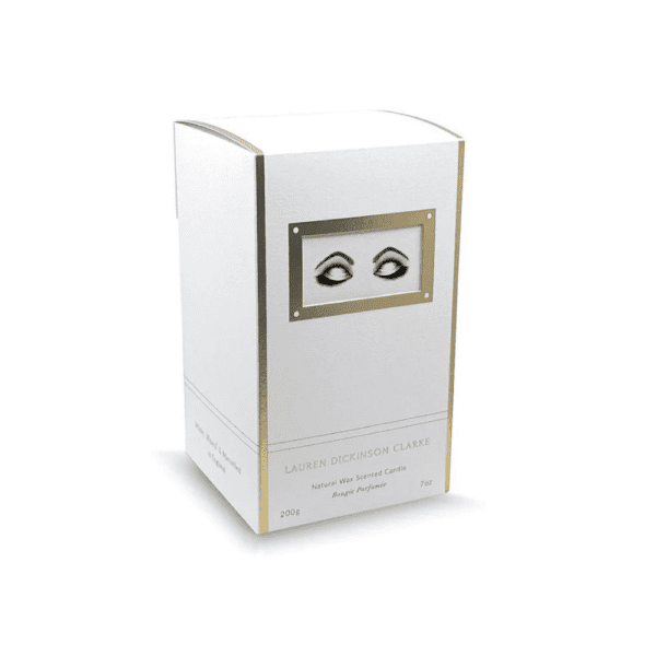 Die Verpackung der Kerze hat eine weiße Farbe mit goldenen Akzenten und ist mit einem Design versehen, das Augen darstellt, die Entspannung ausdrücken.
