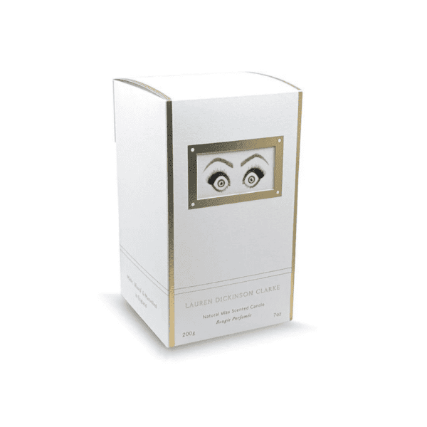 Die Verpackung der Kerze hat eine weiße Farbe mit goldenen Akzenten und ist mit einem Motiv versehen, das Augen darstellt, die Erstaunen ausdrücken.