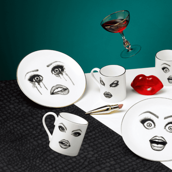 Une collection de vaisselle ornée de visages personnalisés et d'expressions faciales captivantes s'anime sur une table blanche, contrastant magnifiquement avec le fond du mur bleu.