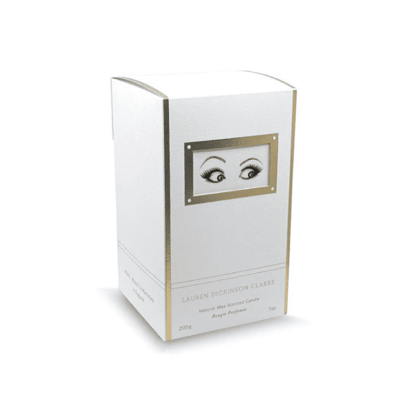 The candle's packaging is white with gold accents, and features a drawing of questioning eyes.