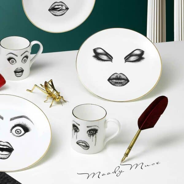 A collection of tableware adorned with personalized faces and captivating facial expressions comes to life on a white table, contrasting beautifully with the blue wall background.