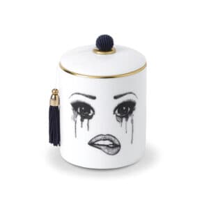 A scented candle in white Chinese porcelain features a melancholy face, carefully traced in felt. The face expresses sadness with flowing tears and melting make-up, while the lower lip is delicately bitten, creating a moving and artistic composition.