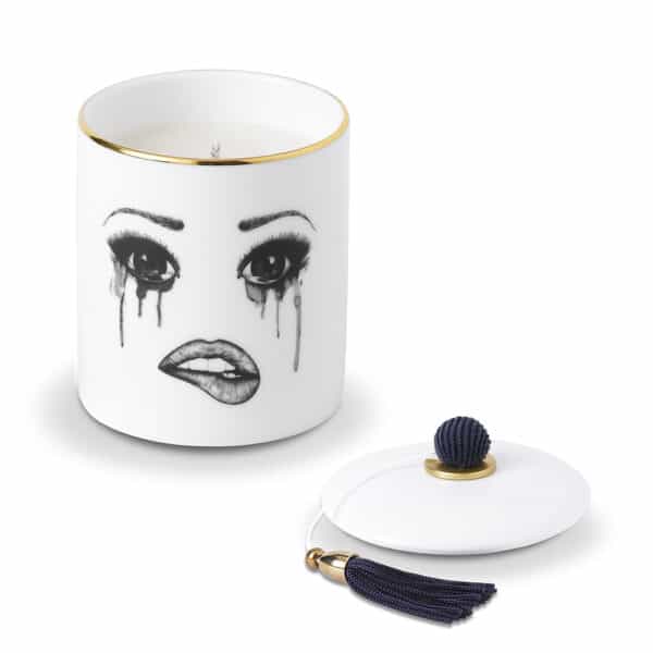 A scented candle in white Chinese porcelain features a melancholy face, carefully traced in felt. The face expresses sadness with flowing tears and melting make-up, while the lower lip is delicately bitten, creating a moving and artistic composition.