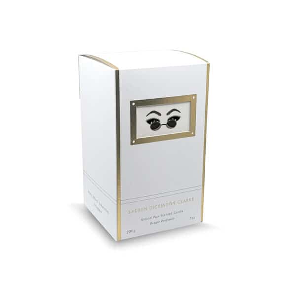 Candle packaging in white with gold finish, adorned with a motif of eyes behind glasses.