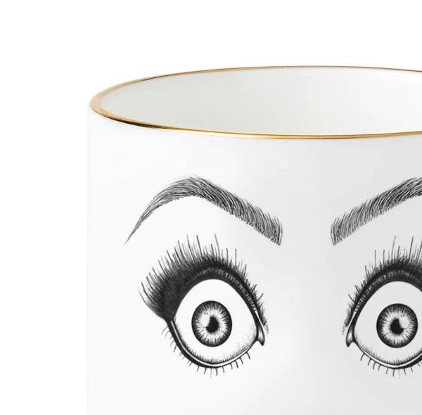 Detalle de una taza de porcelana china blanca con un dibujo de fieltro negro que ilustra una cara sorprendida con ojos muy asombrados y boca abierta, todo ello realzado con detalles dorados.