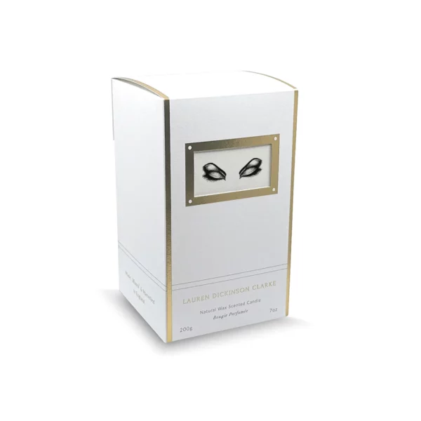 The candle's packaging features a white hue enhanced by gold elements, adorned with a motif featuring closed eyes.