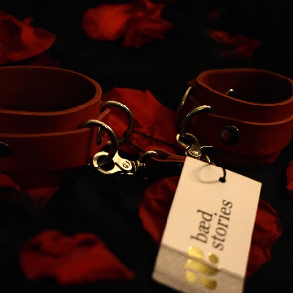 Baed Stories red BDSM handcuffs on black background with red petals.