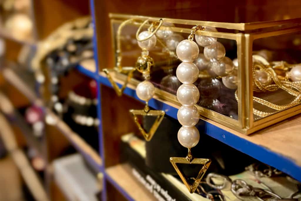 Perlenbesetzte Handschellen mit einem eleganten Dreieck und an einer zarten Goldkette ruhen sanft in einem goldenen Glaskasten, der in einem Notariatsmöbel aus Holz eingebettet ist, das in einem bezaubernden Blauton gestrichen ist.