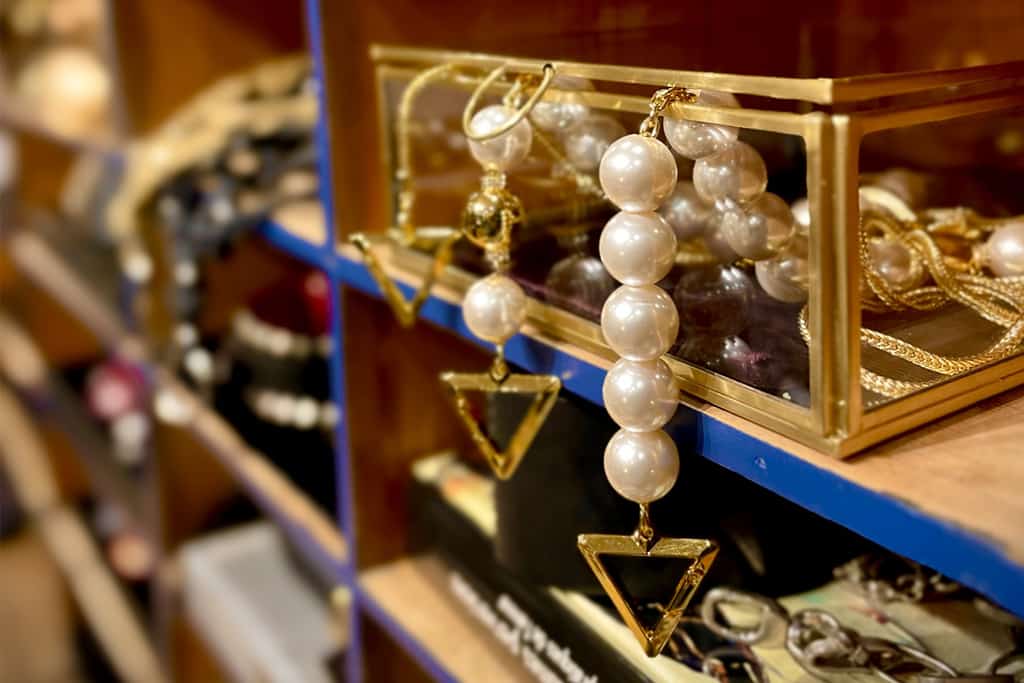 Handcuffs adorned with pearls, embellished with an elegant triangle and suspended from a delicate gold chain, rest delicately in a glass box with golden accents, nestled in the heart of a wooden notary's cabinet painted a delightful shade of blue.