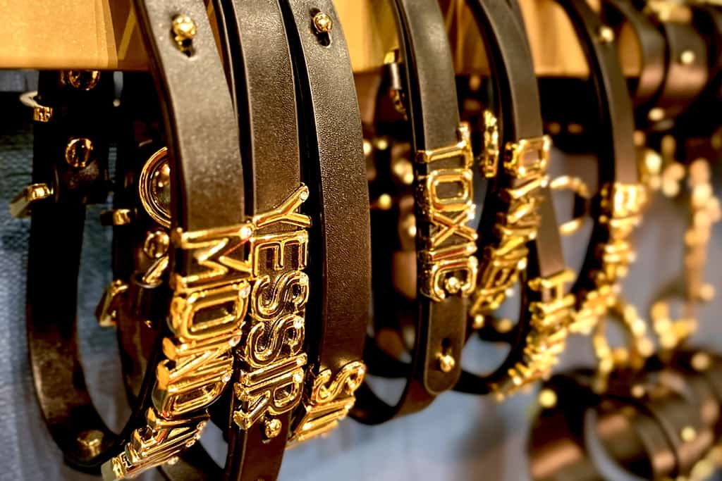 A series of close-up photographs features black leather necklaces adorned with gold lettering. The first necklace proudly bears the word "Mondaine", the second displays a bold "Yessir", while the fourth reveals the intriguing "Toxic".