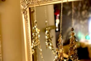 Close-up photograph of a gold accessory. This is a bra made with gold diamonds and gold chains. It is placed on a mirror with gold outlines. The gilded wall can also be seen in the background.