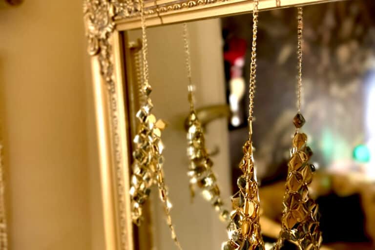 Primer plano de un accesorio de oro. Se trata de un sujetador realizado con diamantes de oro y cadenas de oro. Está colocado sobre un espejo con contornos dorados. Al fondo también se ve la pared dorada.