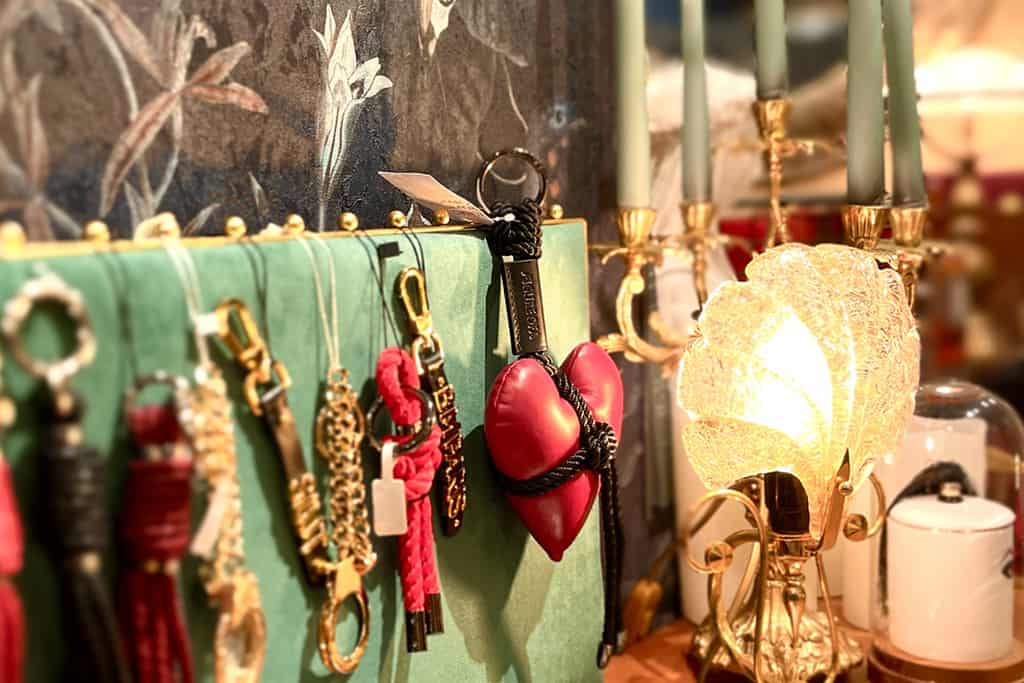 One photograph shows a green suede rack, on which rest various accessories: a leather heart, black leather racks adorned with gold writing, and small gold handcuffs suspended from gold chains.