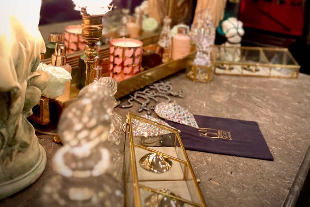 "A close-up photograph highlights a marbled piece of furniture, on which rest two glass boxes with gold detailing. Next to this, a black pouch displays gold lettering. Several accessories are also neatly arranged on this piece of furniture."