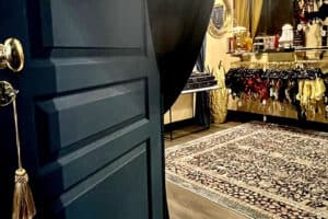 Fotografía de una habitación con una puerta azul en primer plano, una gran alfombra estampada detrás y lencería colgada de barras.