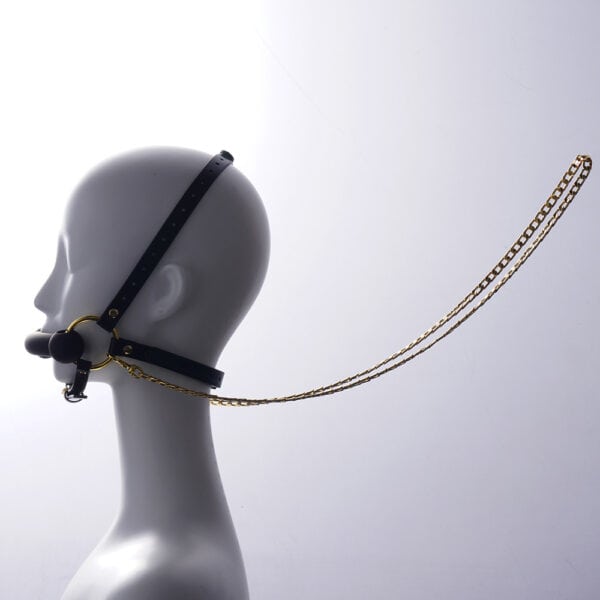 Verstellbares Kopfstützengeschirr und Knebel aus schwarzem Leder, verziert mit goldenen Ringen und Ketten, wird auf einer unbeweglichen weißen Schaufensterpuppe im Profil präsentiert, die mit einem hellen Hintergrund unterlegt ist.