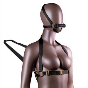 Adjustable harness for headrest and body, with black leather gag and reins attached to the bust, adorned with gold rings and chains, is presented on an immobile mannequin in front of a white background.