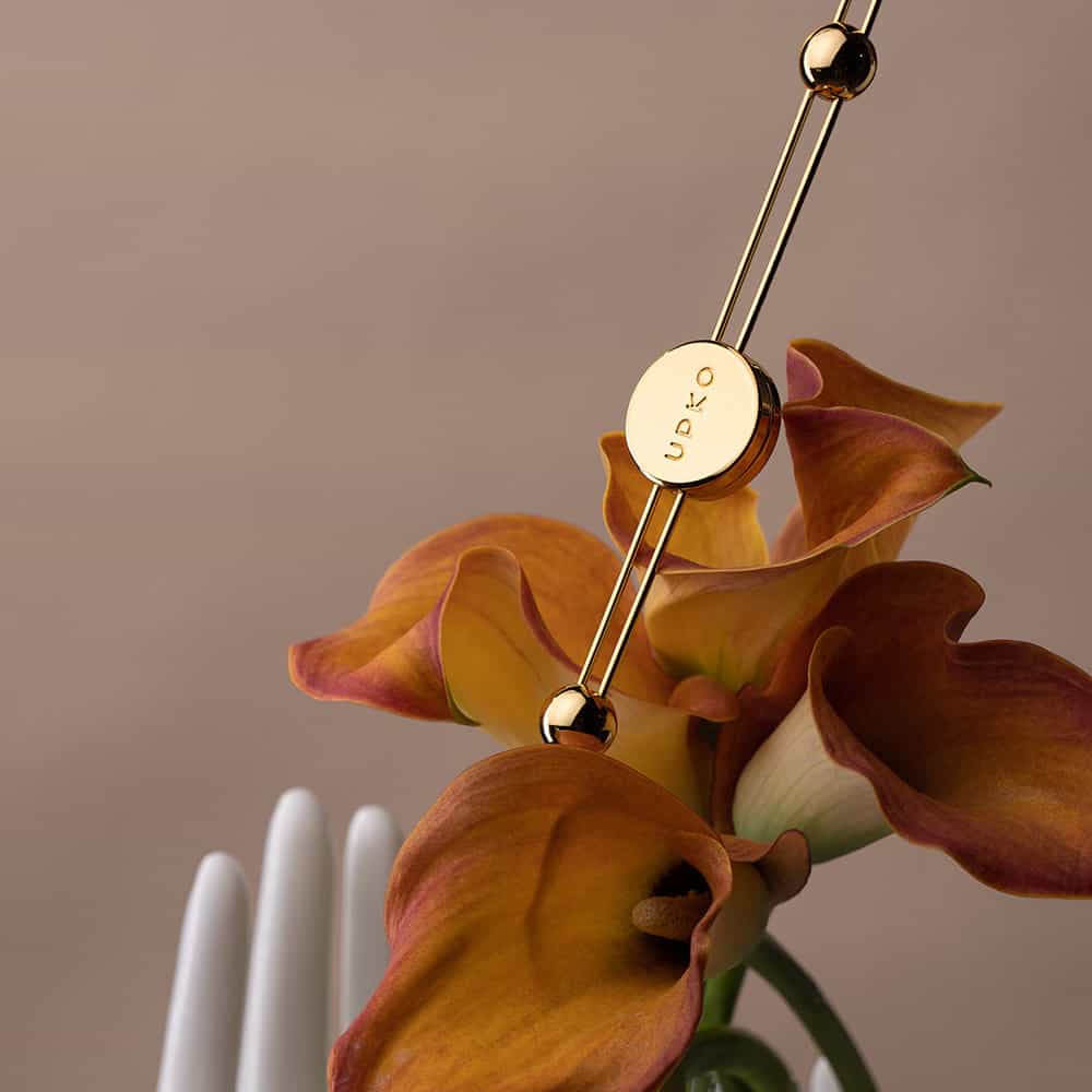 Photographie sur fond marron présentant une barre pinces à tétons dorée posée sur une fleur orange.