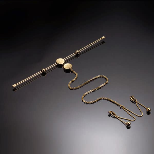 Photo on black background showing a nipple clamp bar with gold-colored clitoral chain.