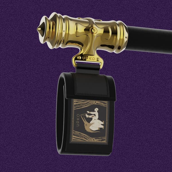 Fotografie auf violettem Hintergrund, die das Ende der Spreizstange mit dem Armband für das Handgelenk zeigt. Das Armband ist schwarz mit dem Markenlogo und ist mit dem goldenen Ende der Spreizstange verbunden.