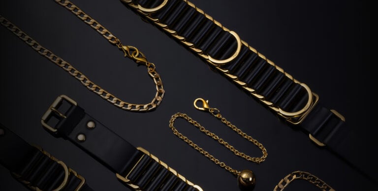 Esta fotografía muestra un conjunto bondage negro con cinturón y cadenas doradas.
