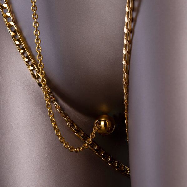 Fotografía en maniquí de una cadena de clítoris con una bola de placer, las cadenas son doradas.