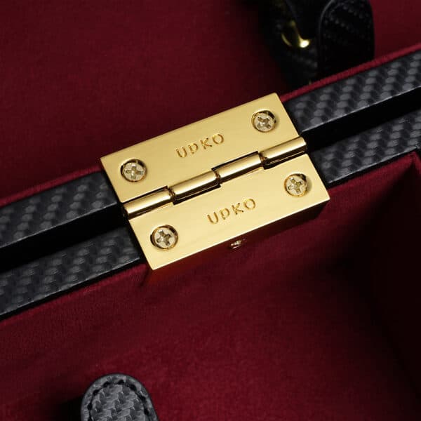 Zoom-Foto vom Inneren des Koffers aus schwarzem Leder mit einem Boden aus rotem Samt. Man sieht eine goldene Plakette mit dem Namen der Marke.