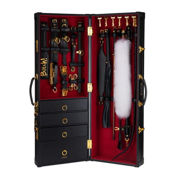 Photograph on a white background showing a black leather trunk with a red velvet interior, gold details and drawers. There are several leather accessories inside.