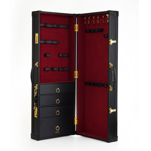 Photographie sur fond blanc montrant une malle noire en cuir avec un intérieur en velour rouge, des détails dorés et des tiroirs.