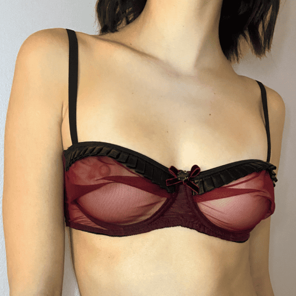 A woman's upper body in a transparent red bra with baked curtains and velvet bows with crystal and black straps.