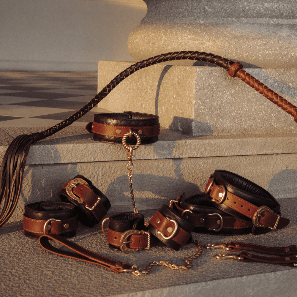 Photograph in front of a wall of various BDSM accessories from The Equestrian by Liebe Seele range, including handcuffs, collars and leashes.