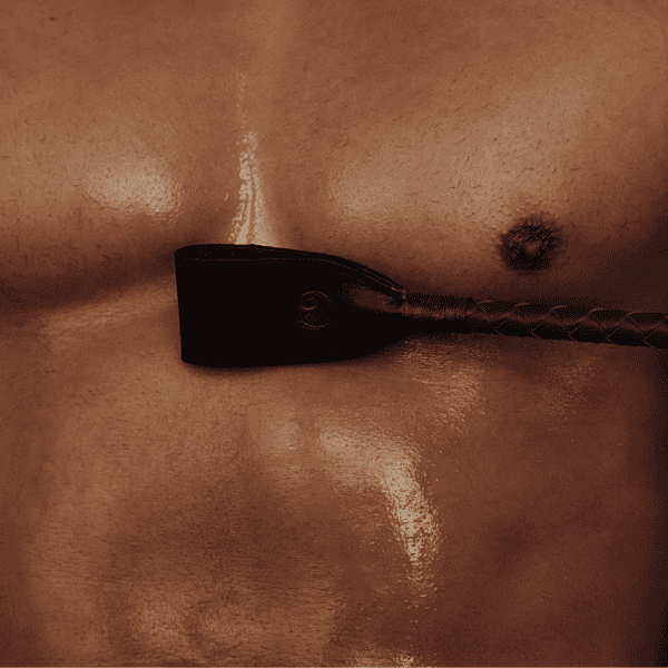 Naked torso of a sweaty, muscular man with a riding crop between his pecs