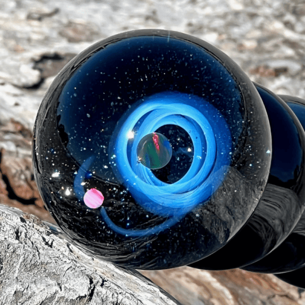 Photographie du dildo galaxie noir sur un tronc d'arbre, bleu nuit avec constellations et planète verte en lévitation