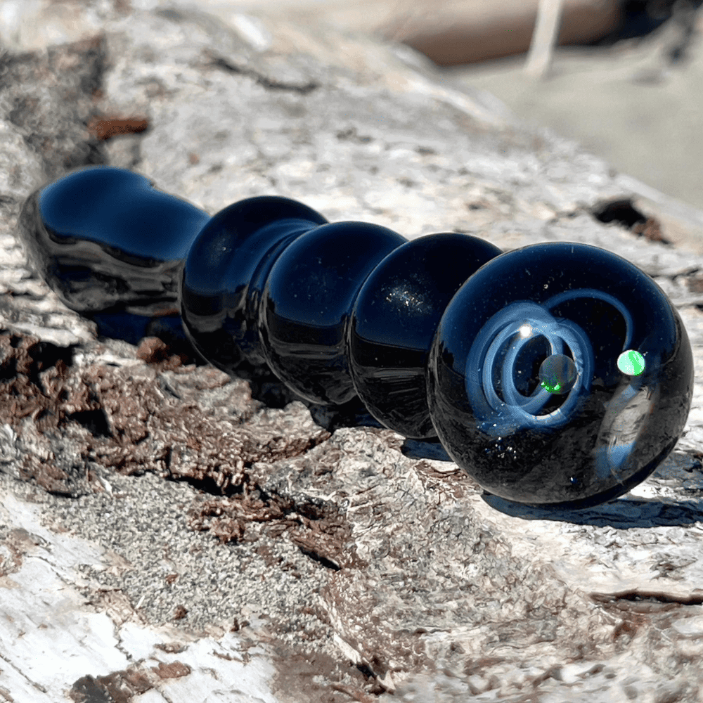 Photographie du dildo galaxie noir sur fond blanc, bleu nuit avec constellations et planète verte en lévitation