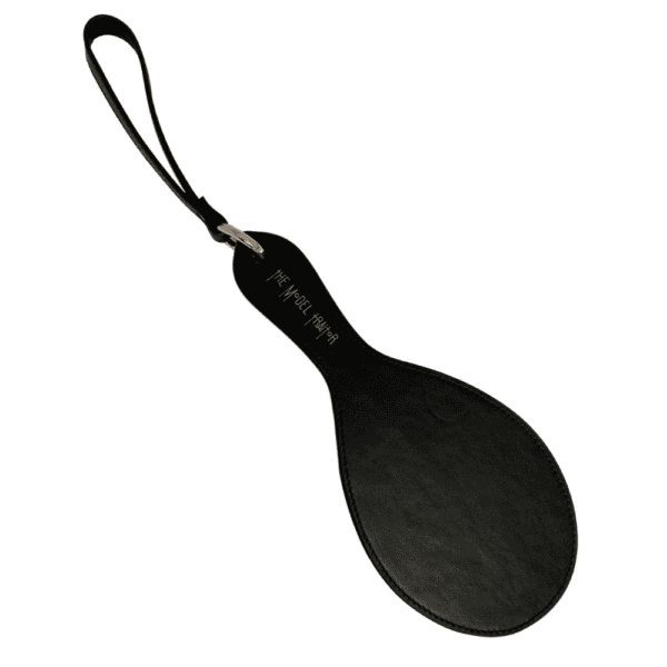 Fotografie auf weißem Hintergrund des Paddle Fessée Leder in schwarzer Farbe mit goldenen Details