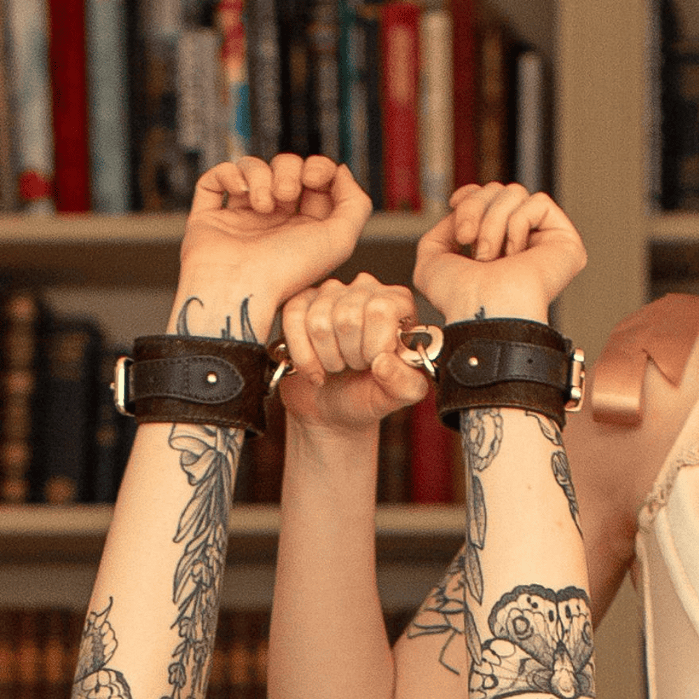 Photograph of a woman who is held by one hand with and has on her wrists Chocolate brown leather cuffs and gold details