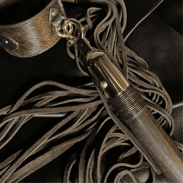Photography on black textile background, accessories bdsm restraint bar and brown leather whip and gold details as chains