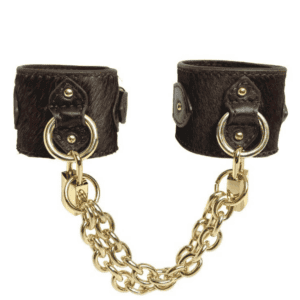 Packshot of the handcuffs seen from the front, they are brown leather with bristles and gold rings, padlocks and chains.