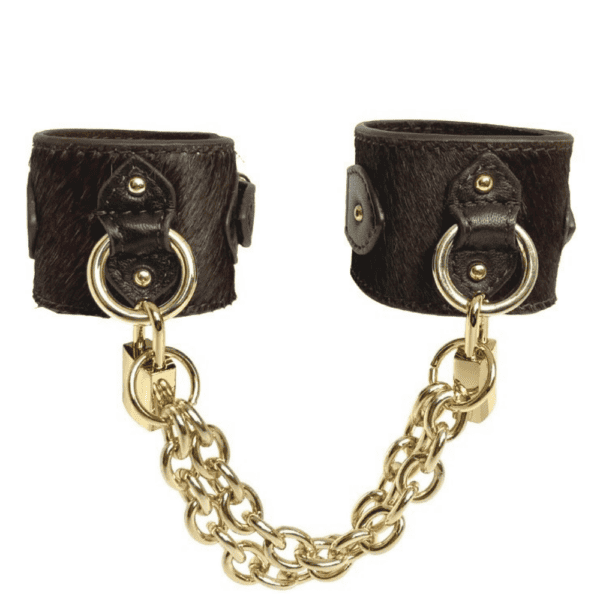 Packshot of the handcuffs seen from the front, they are brown leather with bristles and gold rings, padlocks and chains.