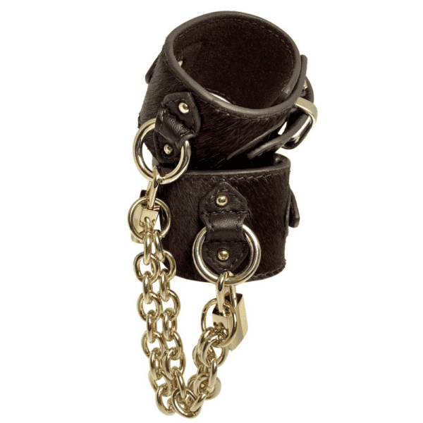 Packshot of the handcuffs seen from the front, they are brown leather with bristles and gold rings, padlocks and chains.
