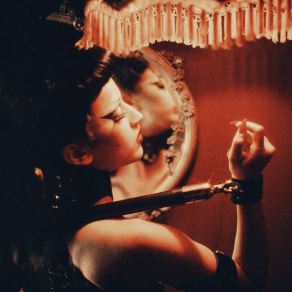 Photographie aux couleurs chaude, une femme maquillé devant un miroir elle est menotté et attaché à une barre d'écartement