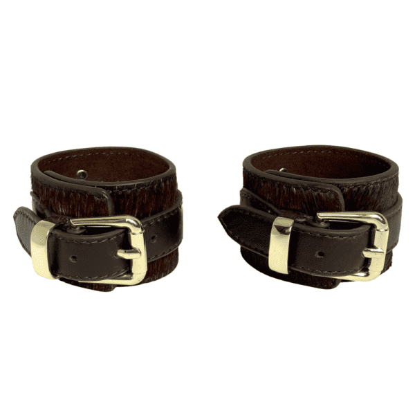 Packshot of the handcuffs seen from the front, they are brown leather with gold bristles and fasteners.