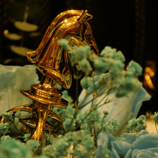 Photographie d’un cavalier en or d’un jeux d’échecs sex toy posé dans un bouquet de fleurs bleus