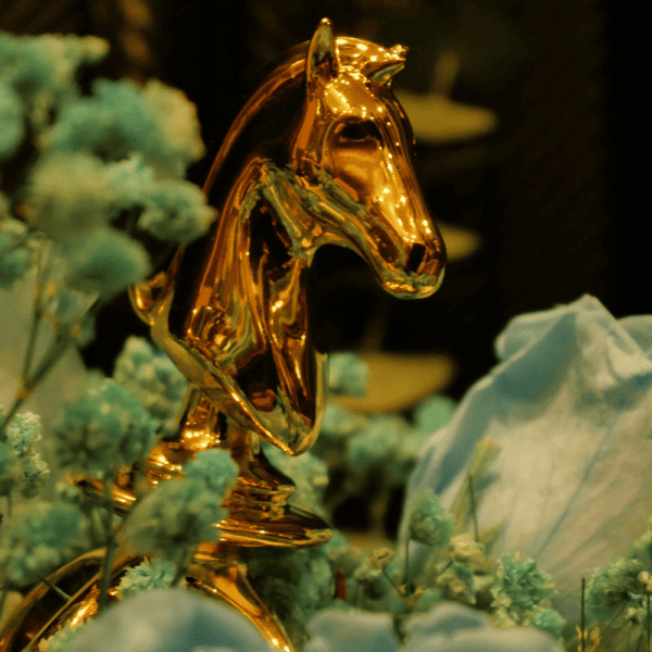Photographie d’un cavalier en or d’un jeux d’échecs sex toy posé dans un bouquet de fleurs bleus