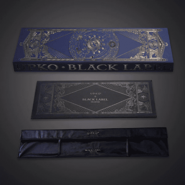 Grey background photograph of blue and gold packaging, box with velvet pouch inscribed "UPKO BLACK LABEL COLLECTION".