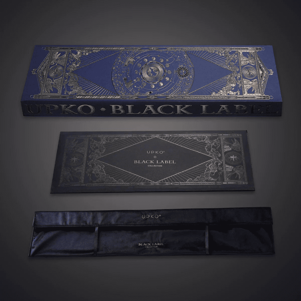 Grey background photograph of blue and gold packaging, box with velvet pouch inscribed "UPKO BLACK LABEL COLLECTION".