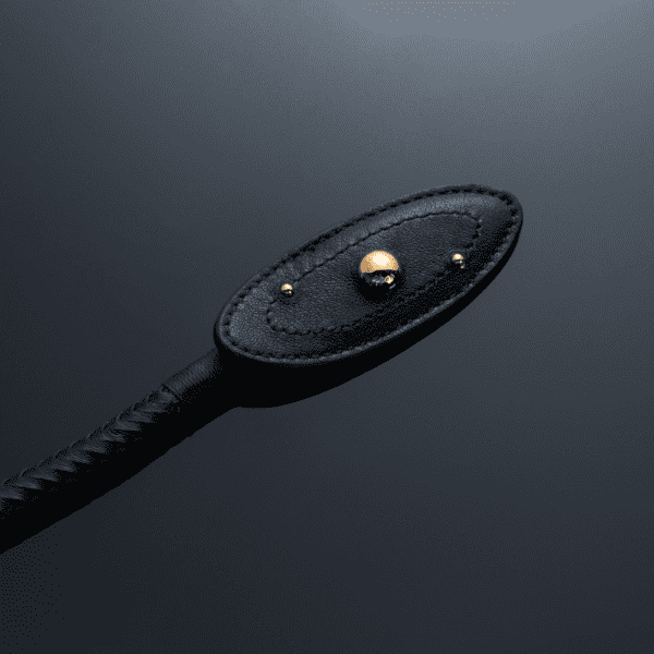 Zoom in on the tip of the whip set against a light-reflecting black background, gold ball details, perfect stitching and braided handle.