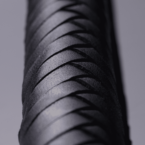 Photographie zoomé et focus sur le manche en cuir tressé noir du fouet posé sur un fond blanc